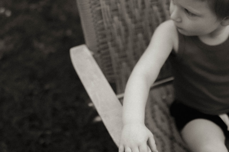 a black and white fine art photograph of a little boy sitting in a lawn chair, by Minnesota based family photographer Kayla Schiltgen